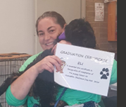 Sarah is smiling and has brown hair. Sarah is holding a dog and a graduation certificate